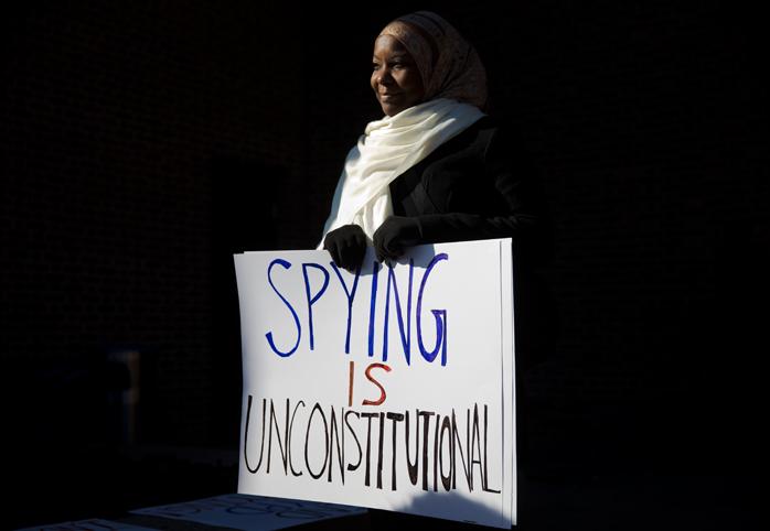 A woman holds a sign that reads "spying is unconstitutional"